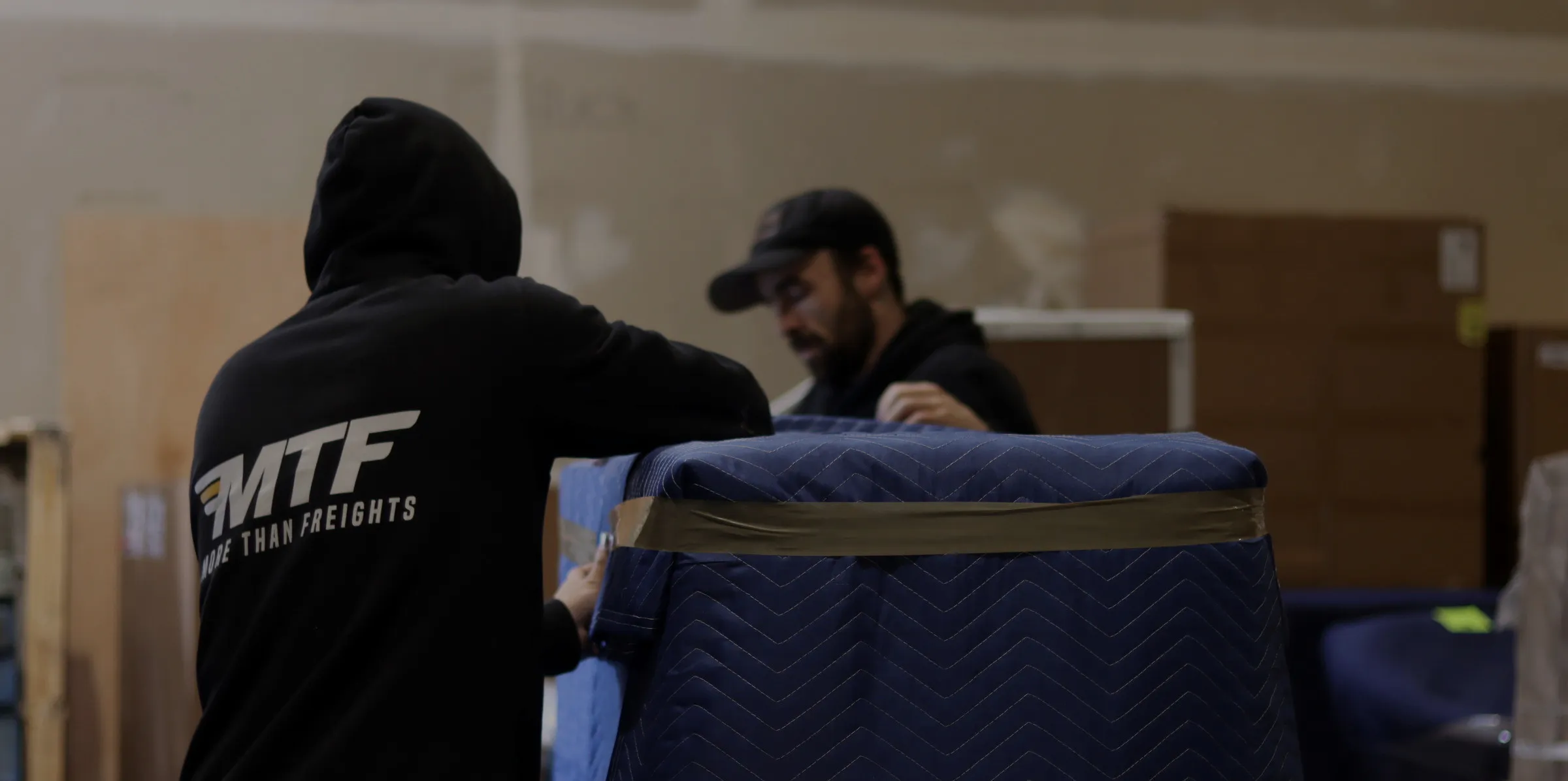 MTF crew members receiving and inspecting a wrapped furniture piece in the warehouse