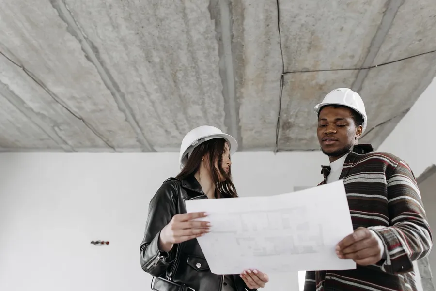 Two architects in hard hats reviewing blueprints on a construction site