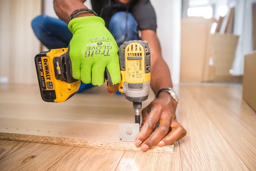 Installer in work gloves using a power drill to assemble furniture